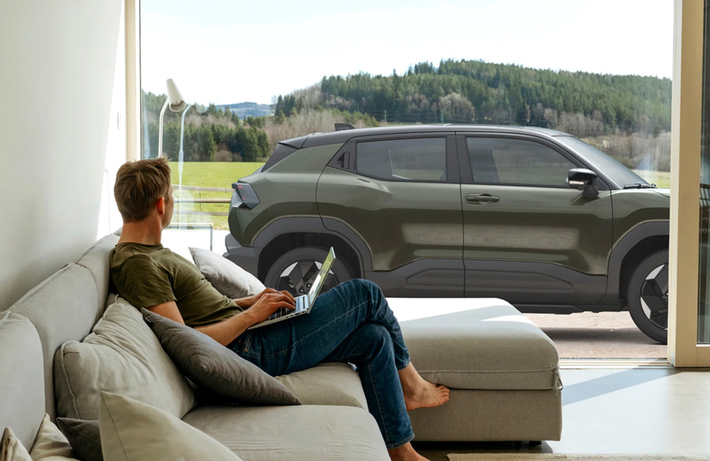 A man sitting on a couch looking longingly out a window at his green Suzuki SUV